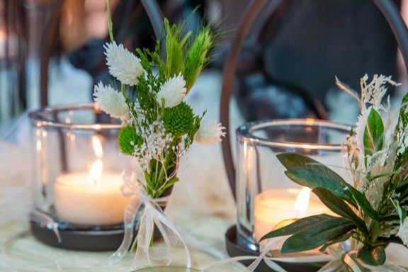 Zwei Kerzen in Gläsern mit Pflanzen dekoriert