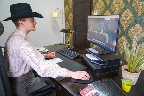 Mitarbeiter der Westernstadt Pullman City in authentischer Westernkleidung sitzt vorm Computer und arbeitet
