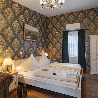 Gemütliches Doppelzimmer mit luxuriösem Dekor und warmem Licht Ein stilvolles Schlafzimmer mit eleganter Tapete, einem großen Bett und einem gemütlichen Sessel in der Ecke.